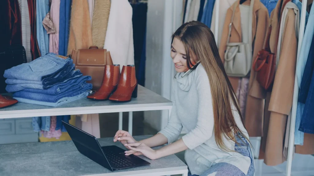 Een eigenaar van een kledingwinkel staat een klant telefonisch te woord terwijl ze iets opzoekt op haar laptop