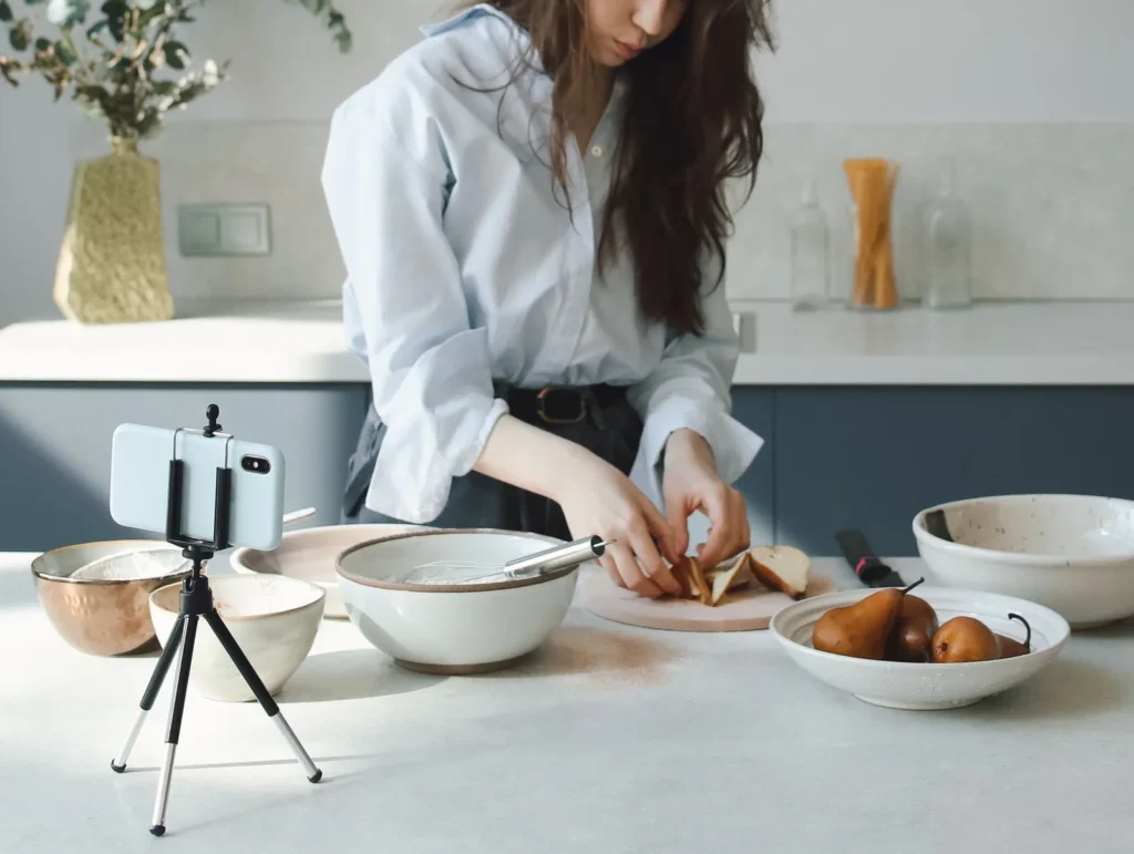 Vrouw bereidt peren in een lichte keuken terwijl een smartphone op een klein statief haar filmt