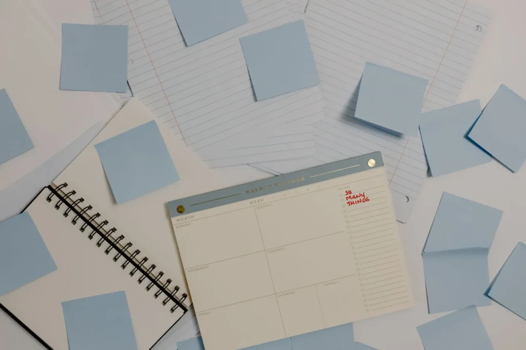 Een lege weekplanner tussen lichtblauwe plakbriefjes en gelinieerd papier op een bureau