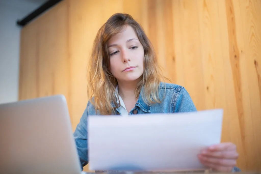 Een jonge vrouw in een spijkerjasje leest aandachtig een document naast haar laptop
