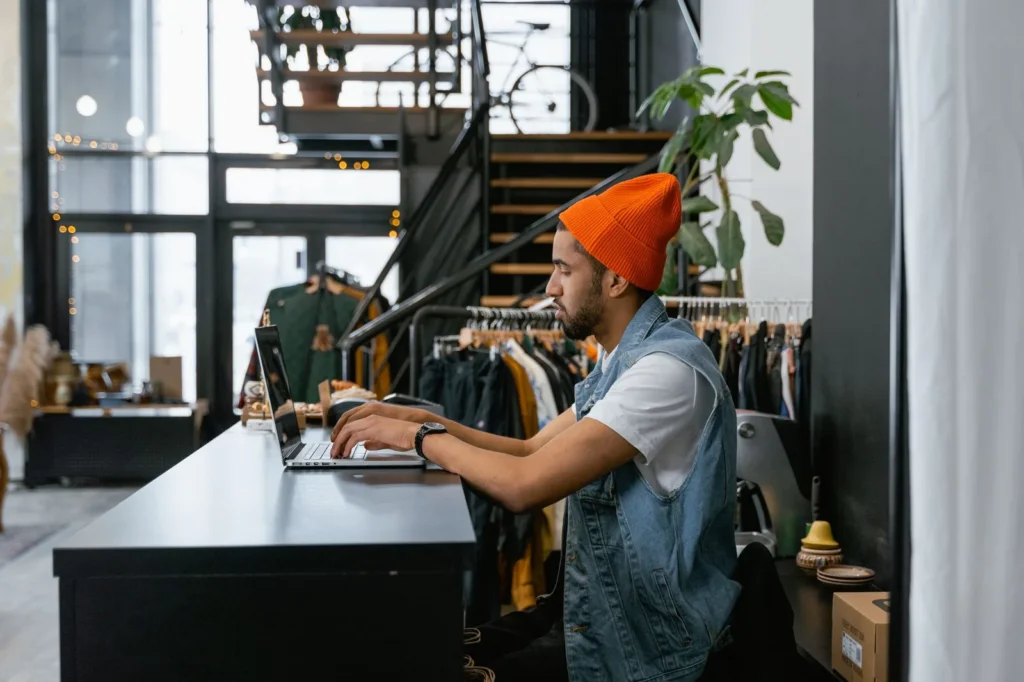 Ondernemer typt op een laptop aan de toonbank van een kledingwinkel
