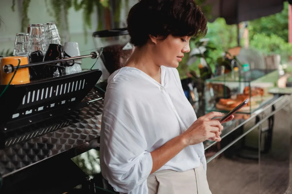 Een ondernemer in haar koffiezaak kijkt op haar smartphone, naast de espressomachine