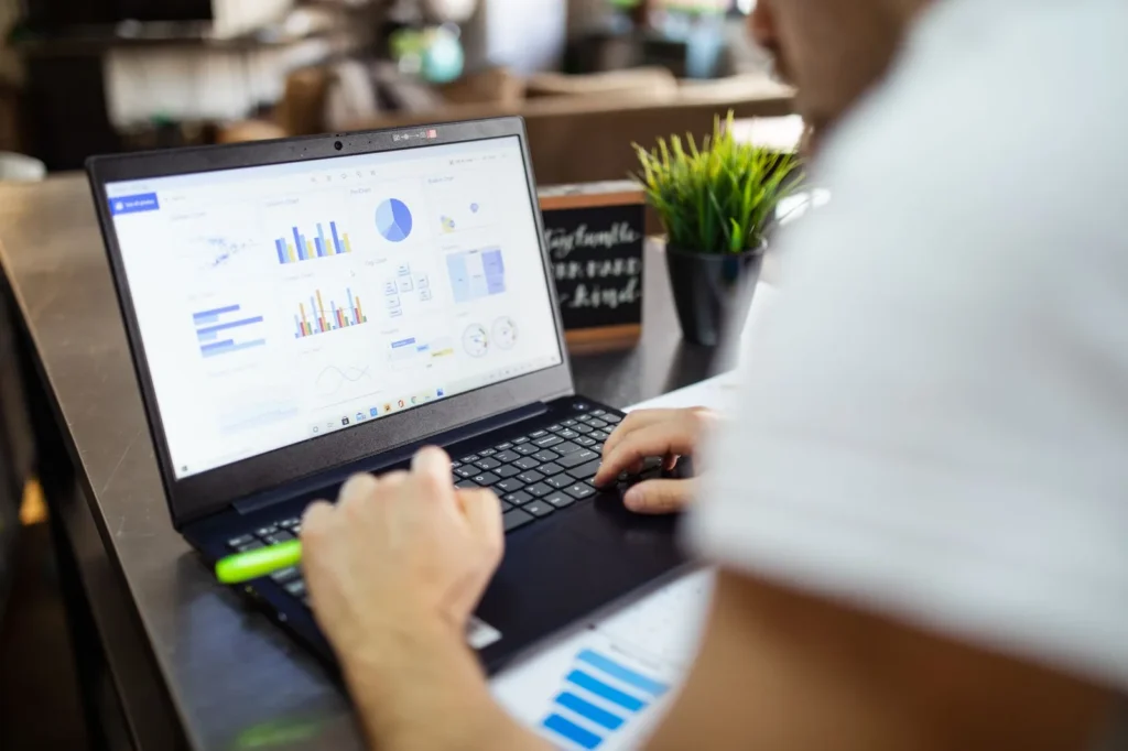 Iemand werkt aan een laptop met een scherm vol grafieken en diagrammen op een houten bar