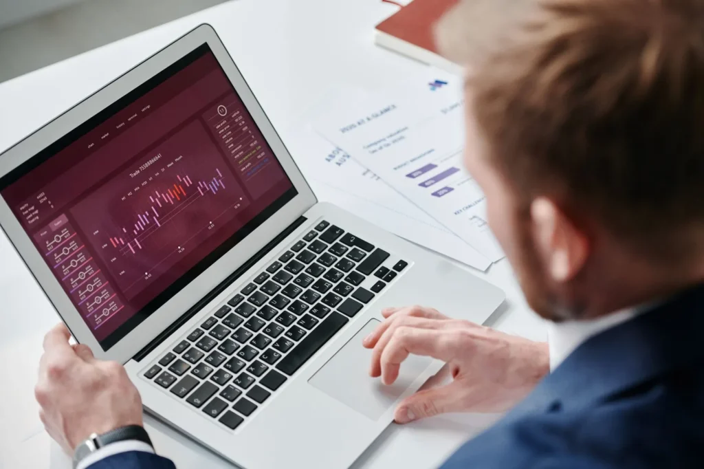 Man in pak bekijkt een dashboard met grafieken op een laptop, met papieren rapporten op tafel