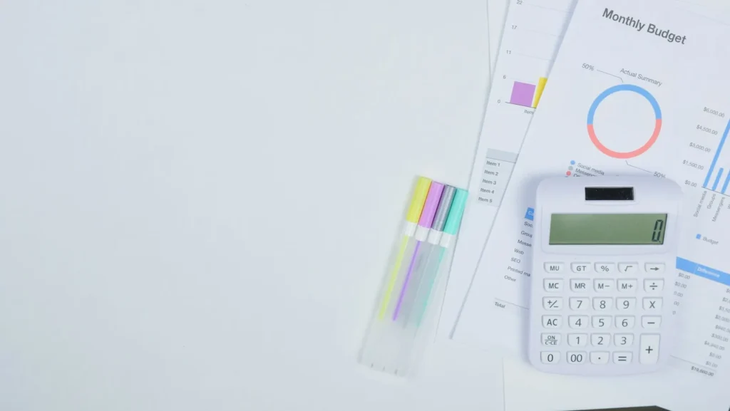 Rekenmachine, markeerstiften en een overzicht van een maandbudget met grafieken op een wit bureau