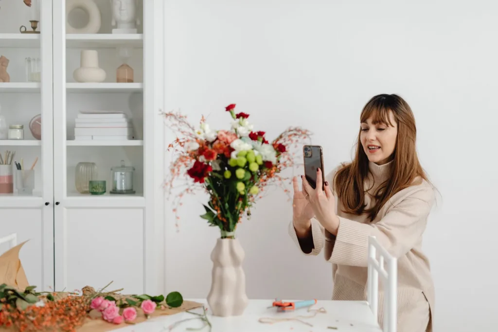 Een bloemist fotografeert een boeket in een vaas met haar smartphone