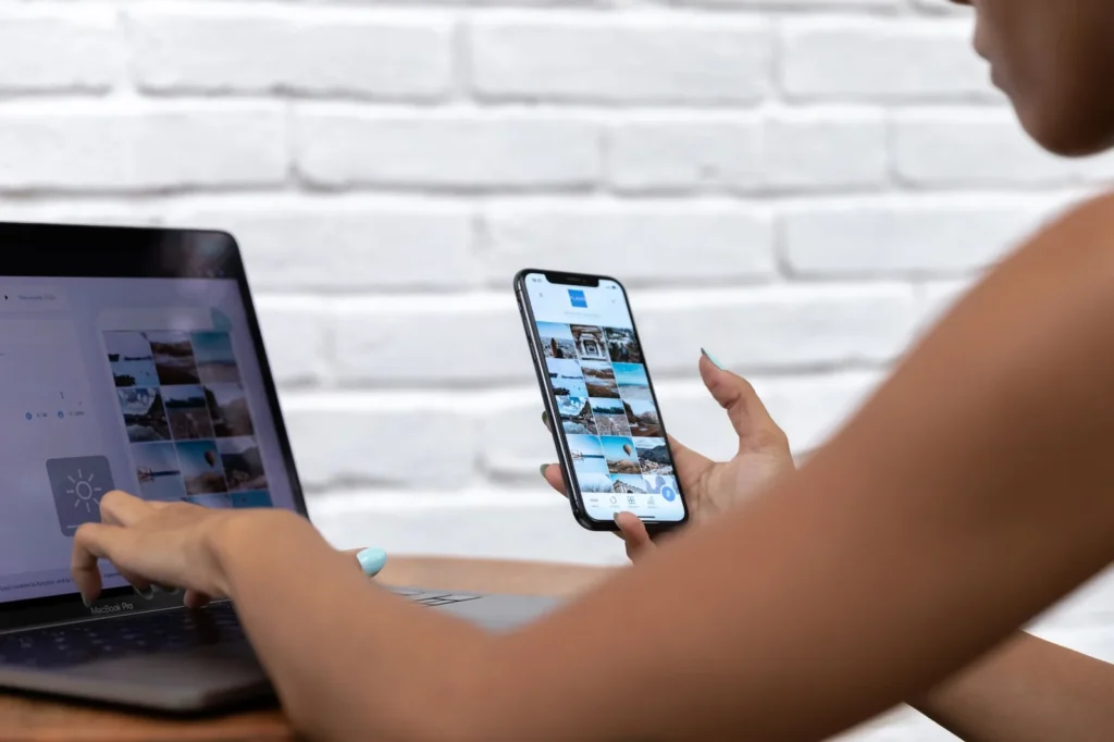 Een vrouw bekijkt een fotofeed op haar smartphone terwijl ze op een laptop werkt