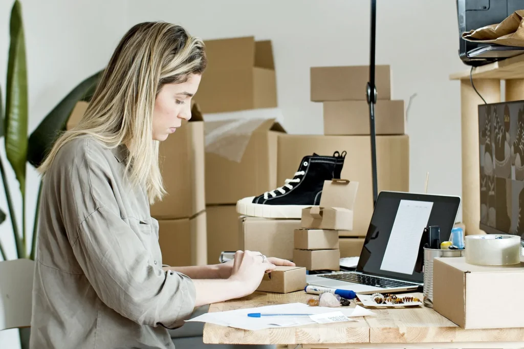Een ondernemer met een webshop pakt een bestelling in aan haar bureau, met een laptop, dozen en een sneaker op de achtergrond