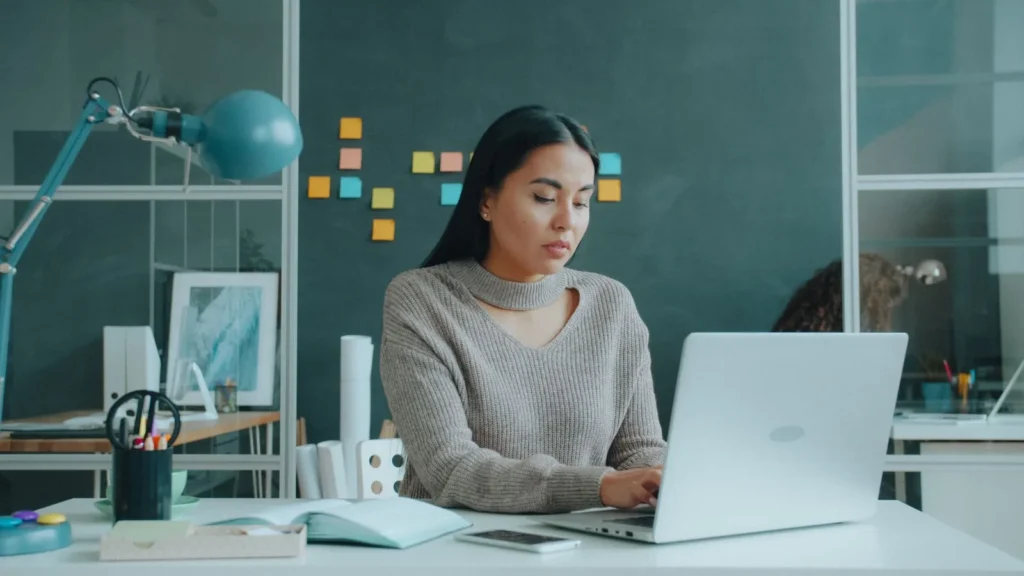 Ondernemer typt op een laptop aan een wit bureau, met gekleurde plakbriefjes op de muur achter haar